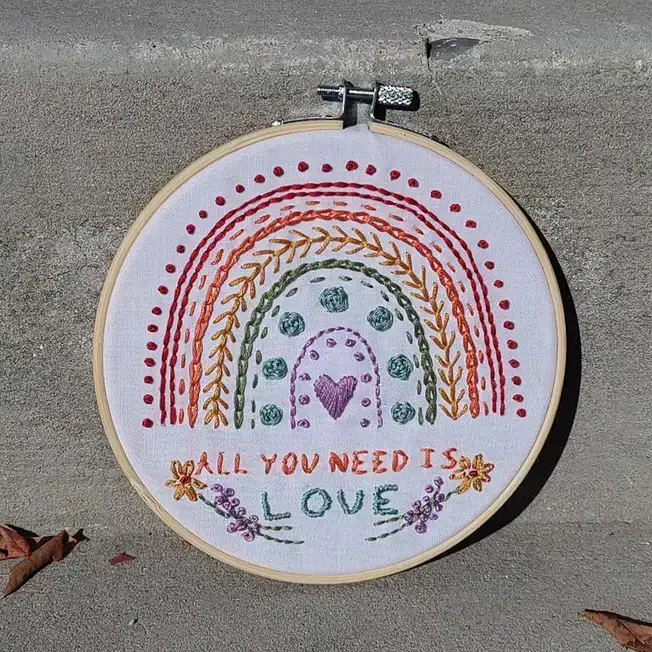 Embroidery of a rainbow with the words 'all you need is love'.